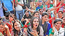 Photo d'une foule de jeunes gens arborant des symboles rouge et vert, au premier plan des femmes non voilées