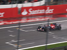 Vettel driving to the left of a light red pit lane barrier on a wet track surface