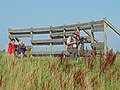 Trois personnes se tenant devant un observatoire d'oiseaux, l'une d'elles tient dans sa main un appareil photo