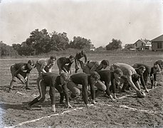 A football team crouching in preparation for a snap on a dirt field