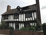 Photo showing the house at Godric's Hollow it has a hole in the roof. There are 3 windows on the second floor. It is a white colour with black beams.