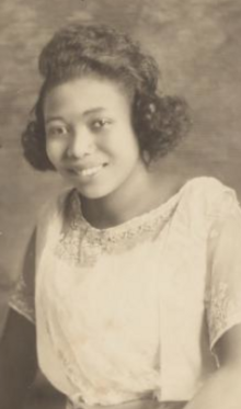 A smiling young Black woman wearing a white dress