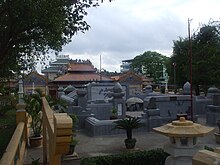 A cemetery with densely packed headstones made of cement. Almost no grass or flora can be seen. Many of the headstones are elaborate with a yellow or orange-tiled roof in the manner of an East Asian temple