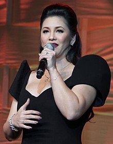 A photograph of woman wearing a black gown singing to a hand-held microphone
