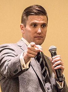 A photograph of Richard Spencer holding a microphone and pointing