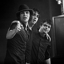 A black-and-white photo of the band embracing and pointing to the camera