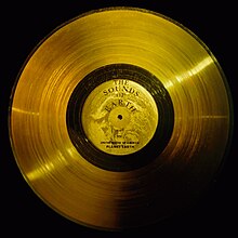Flat circular disc of gold, with a central label, a hole, and a wide band of very small lines, like a golden version of an old analog record
