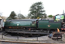 A posed side-and-front view of another large 4-6-2 steam locomotive with a tender stored in a railway station siding. This is another locomotive with flat metal side sheets.