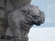 An eroded statue shaped as the front quarters of a rhinoceros. The background is water.