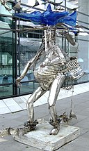 A silver statue of a standing humanoid figure with a blue head made out of shapes.