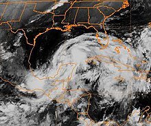 Grayscale image of a disorganized tropical cyclone located at the image's center. The storm appears as a ragged, elongated 's' shaped mass of clouds.