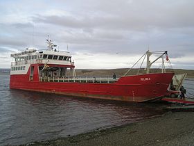 Navire rouge avec une cabine blanche dont la proue est sur une berge