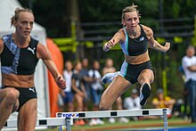 Photo of Femke Bol in the air while passing a hurdle seen from her front