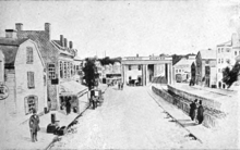 A drawing of a 19th-century city street with a single railroad track running down it. A Greek temple-like station spans the track.
