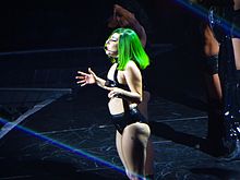 Lady Gaga in a black leather outfit and green wig performs onstage.