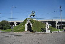 Vue d'un bâtiment circulaire, couvert d'herbe et surmonté d'une statue équestre.