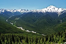 A view from a high ridge over a sweeping forested river valley through mountainous terrain