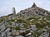 The top of Brown Willy, with many granite boulders, some piled up to form a cairn, next to the trig point
