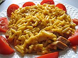 A Canadian meal—Kraft Dinner with added Cheddar that has been integrated with sliced vegetarian hot dog and accompanied by fresh tomato slices