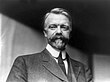 A black-and-white of a man with a mustache wearing a suit and a tie