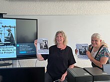 Professors María Mecía and Deena Larsen, holding the "Women Electronic Literature Writers in Wikipedia" Project poster.