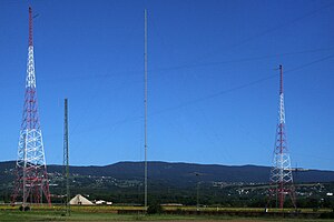 Two metal-truss radio towers against a blue sky.