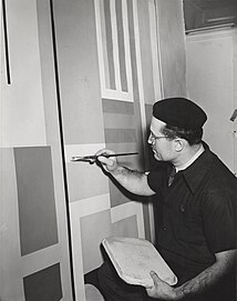 Jean Xceron wearing a beret, painting with a brush while holding a palette