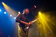 Mike Kinsella with a black electric guitar singing into a microphone