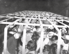 Black-and-white photograph of a cage-like enclosure filled with men.
