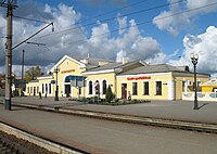 A long beige building with a gray roof with railroad tracks in front