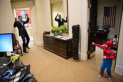 A boy in a Spider-Man costume pretends to shoot out spider webs towards Barack Obama.