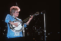 Barbara Mandrell, singing into a microphone while playing a banjo.