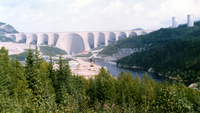 Barrage Daniel-Johnson avec la centrale en bas à droite, le long de la rivière Manicouagan, et les deux cheminées d'équilibre en haut à droite.