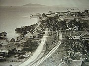 Photographie en noir et blanc d'une ville côtière. Une île montagneuse peut être aperçue à l'horizon.