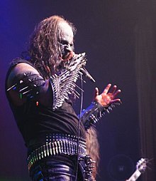 A white man dressed in black holding a microphone.