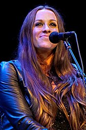 A woman wearing a black leather jacket smiling behind a microphone