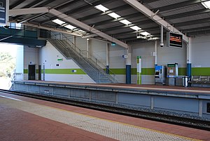 Station platforms with shelter covering the platforms and tracks and stairs heading up to a footbridge