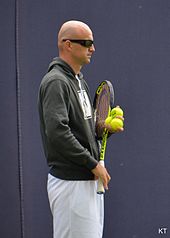 Ivan Ljubičić standing in athletic gear and sunglasses, holding a racquet in his right hand and three balls in his left hand.