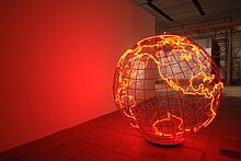 To the right of a red wall, a steel sphere glows along the edges of the Earth's continents.