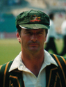 A white-skinned man posing in front of the camera; he is wearing a green cricket cap and shirt