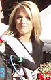 Young blonde woman behind microphone with beauty contestant sash on