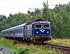 A blue passenger train on a railway running beside a forest