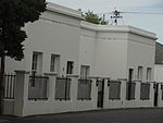 Semi-detached single storey dwellings; parapet wall with plaster mouldings; stippled plaster to walls; painted steel casement windows; stable doors with glazing; new partially enclosed arched porches; low boundary hedge; two adjoining garages. Type of site: House Current use: House.