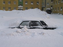 A car buried in a snowdrift with only the left side, from just below the windows, visible