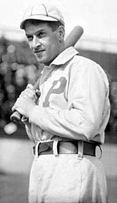 A black-and-white photograph of a man in a white baseball uniform with the letter "P" over the left side of his chest holding a baseball bat over his right shoulder.