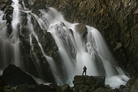 Vue de l'intérieur d'une grotte, avec un homme devant une cascade d'eau.