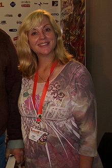 a blonde woman wearing a purple-and-white shirt and a red lanyard