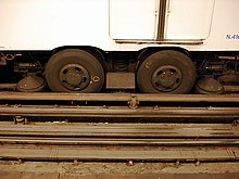 Photographie en couleurs d'un bogie de matériel ferroviaire équipé de roues à pneus.