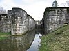 A large canal lock built of limestone, almost entirely empty of water and clearly abandoned