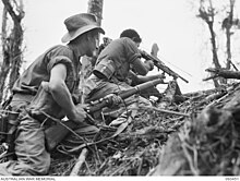 Black and white photograph of two Australian soldiers taking cover behind an embankment. One is aiming his rifle over the top.